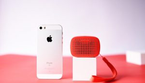 iPhone mit Bluetooth-Lautsprecher auf rotem Untergrund