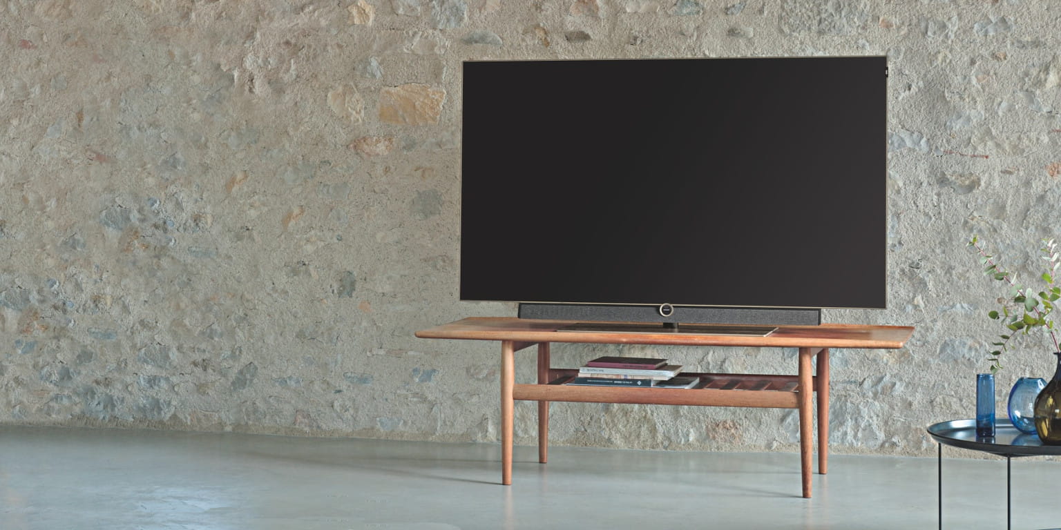 Loewe-TV auf Holztisch vor Steinwand