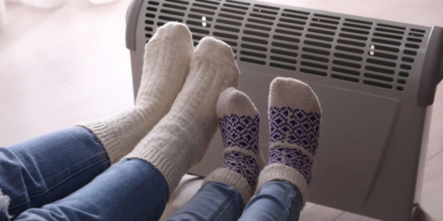 Mutti und Kind wärmen ihre Füße an einer Konvektorheizung
