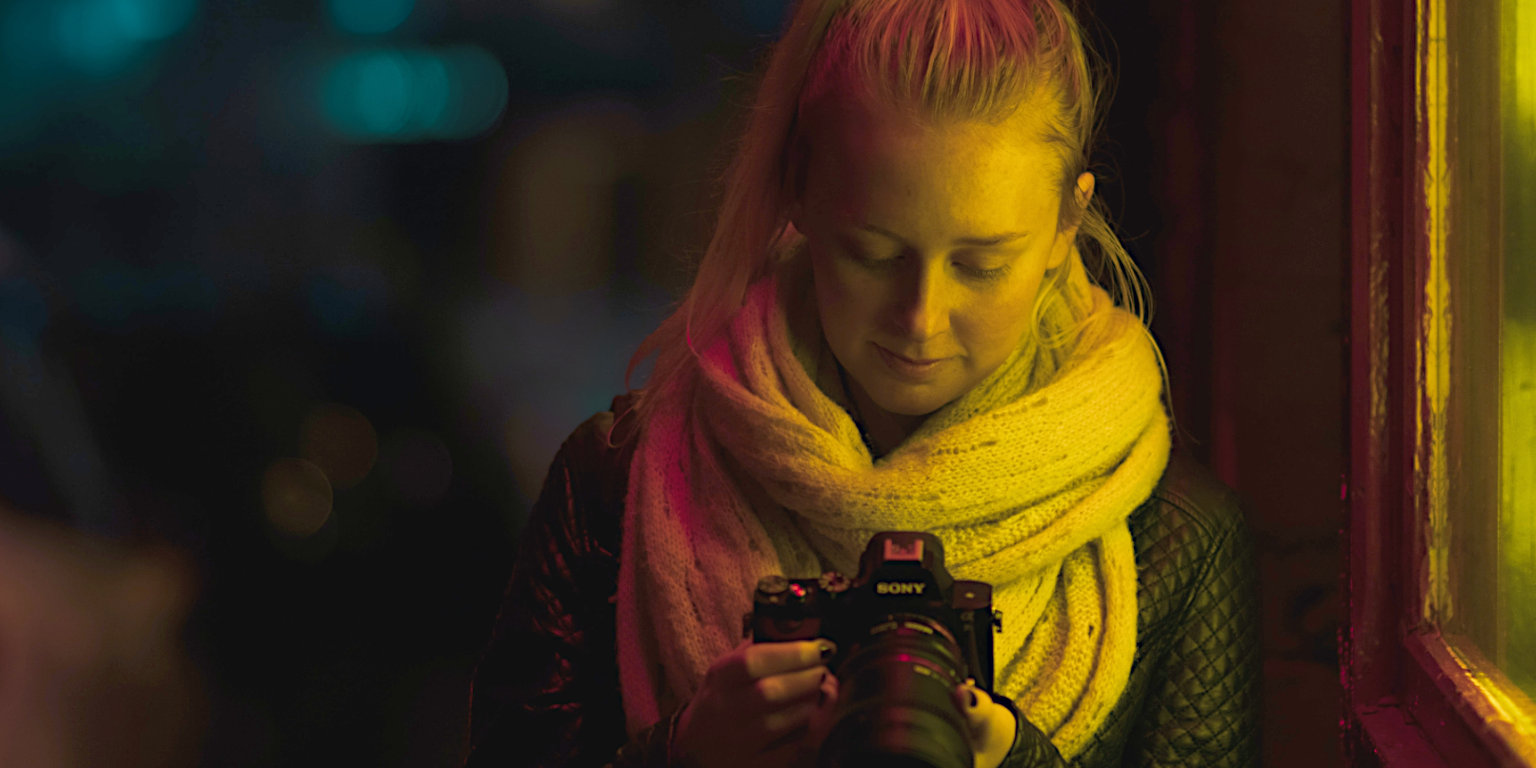 Junge Frau betrachtet eine Sony-Kamera for einem erleuchteten Fenster bei Nacht