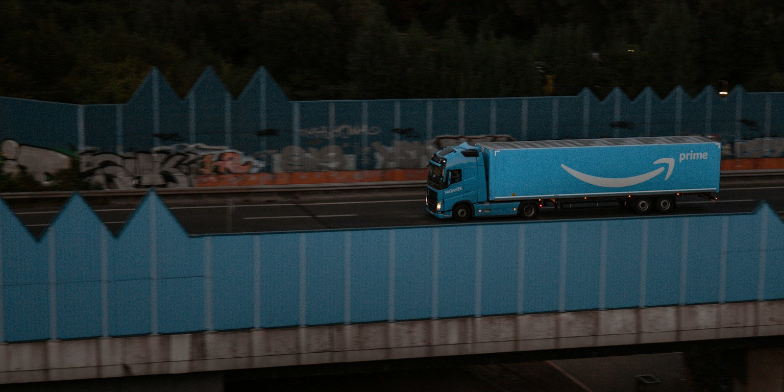 Blauer Amazon Prime Lieferwagen auf Brücke zwischen Zäunen