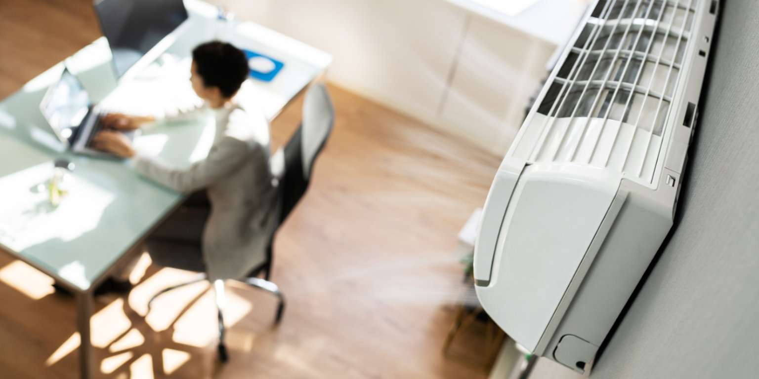 Frau sitzt im Homeoffice Klimagerät hängt an der Wand